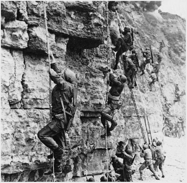 Black-and-white historical photograph of U.S. Army Rangers scaling the steep cliffs at Pointe du Hoc during the D-Day invasion of Normandy on June 6, 1944, using ropes and ladders under enemy fire during World War II.