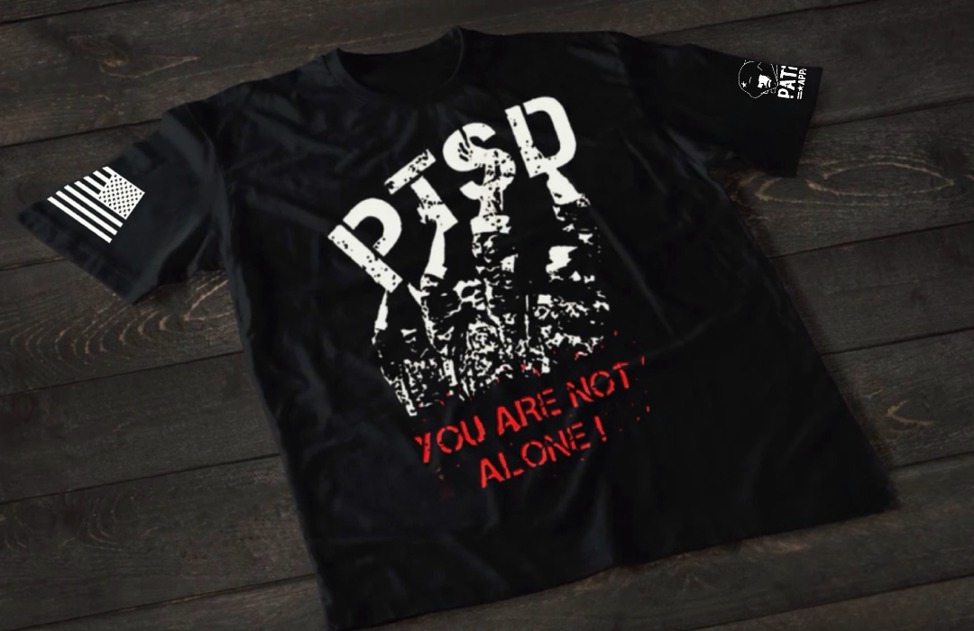 Black patriotic PTSD awareness t-shirt from Patriot Apparel featuring distressed white “PTSD” lettering with military imagery and the message “You Are Not Alone” in red, designed to raise awareness for veteran mental health and PTSD support.
