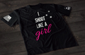 Black women’s I Shoot Like a Girl T-shirt featuring bold white text with pink script lettering and bullet hole graphic accents